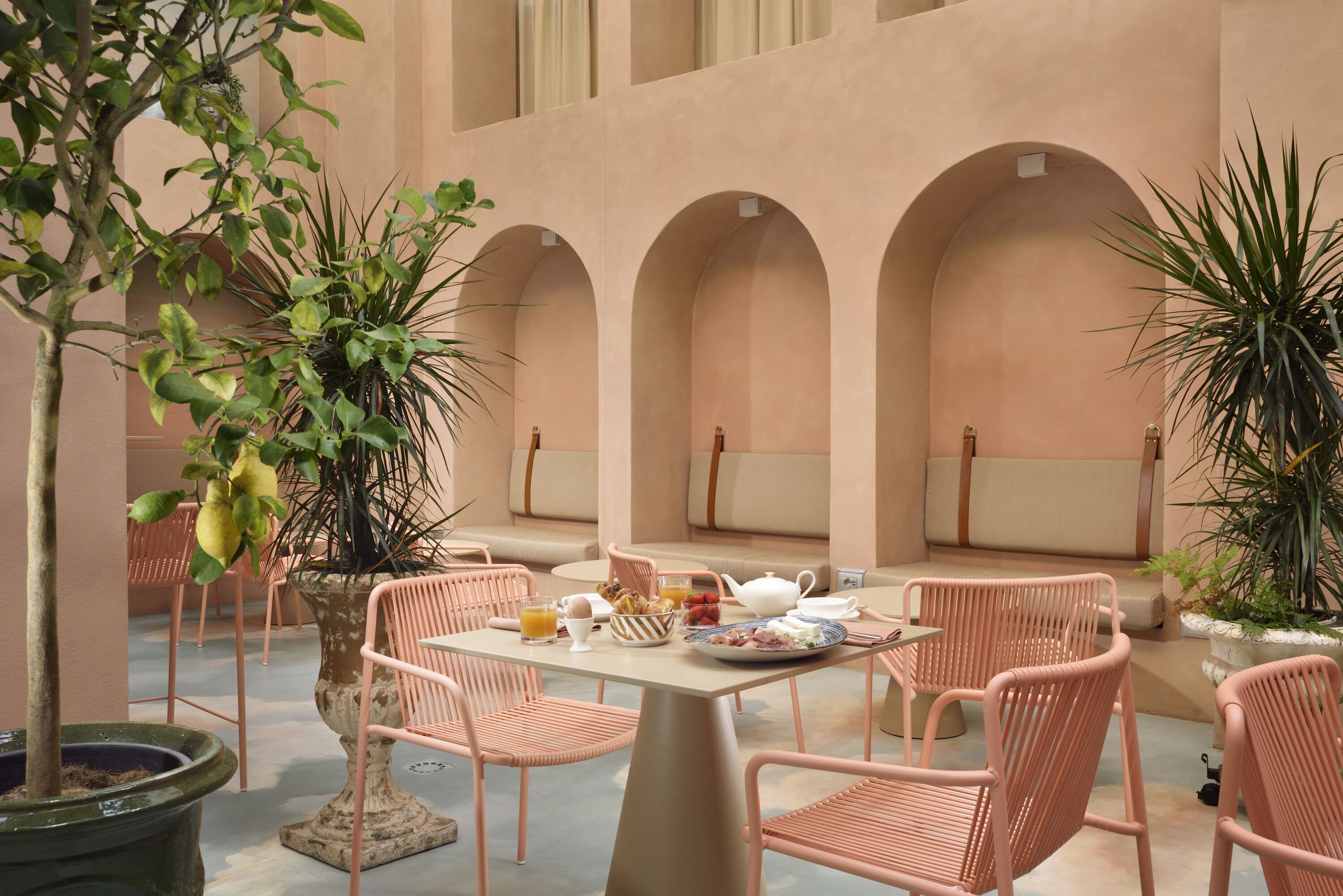 A cozy outdoor seating area with a table set for breakfast, surrounded by cushioned chairs and potted plants.