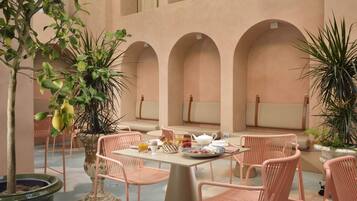 A cozy outdoor seating area with a table set for breakfast, surrounded by cushioned chairs and potted plants.