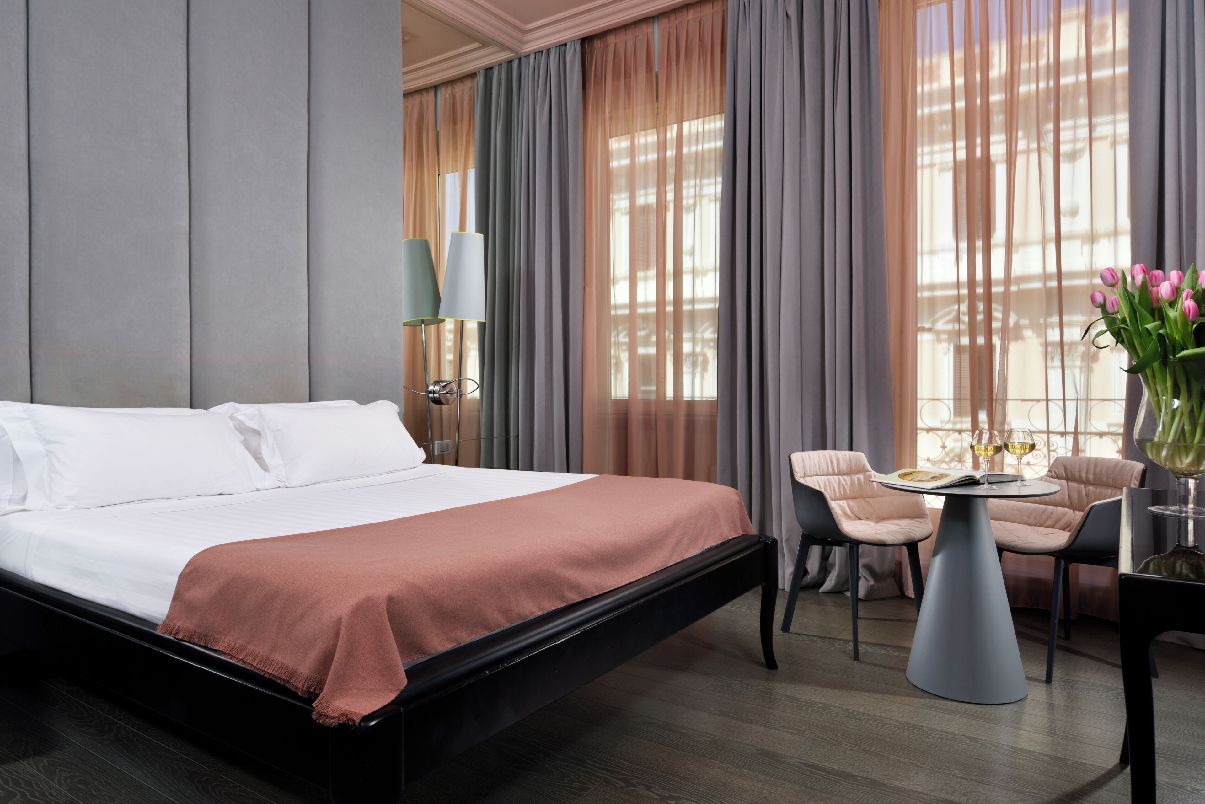 Een hotelkamer met een groot bed, een ronde tafel met stoelen en een bloemenvaas.