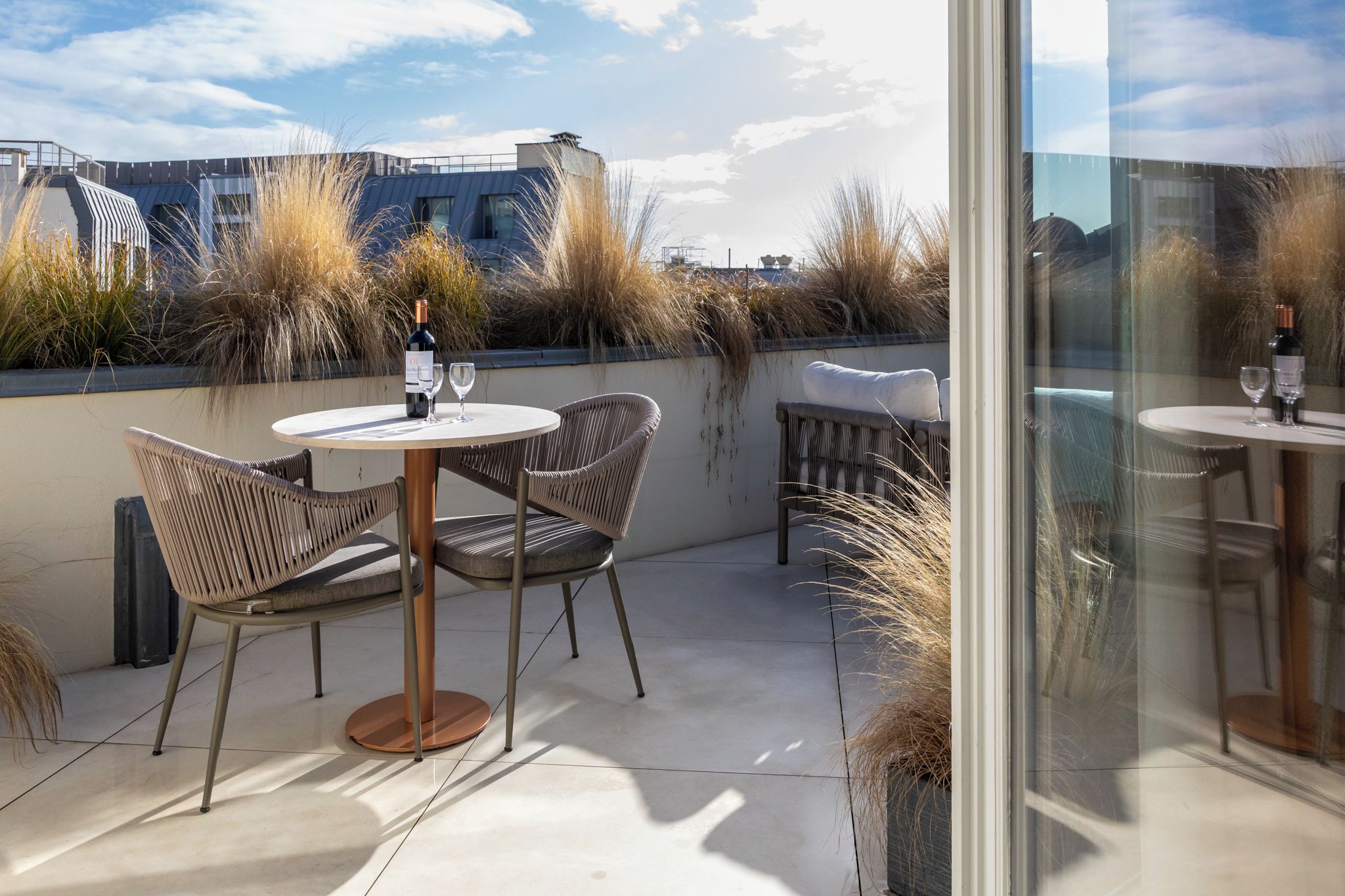 Eine Terrasse im Freien mit runden Tischen und Korbstühlen, einer Weinflasche und einem Glas auf jedem Tisch.