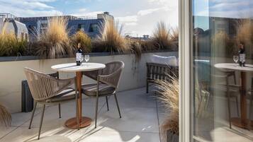 Eine Terrasse im Freien mit runden Tischen und Korbstühlen, einer Weinflasche und einem Glas auf jedem Tisch.