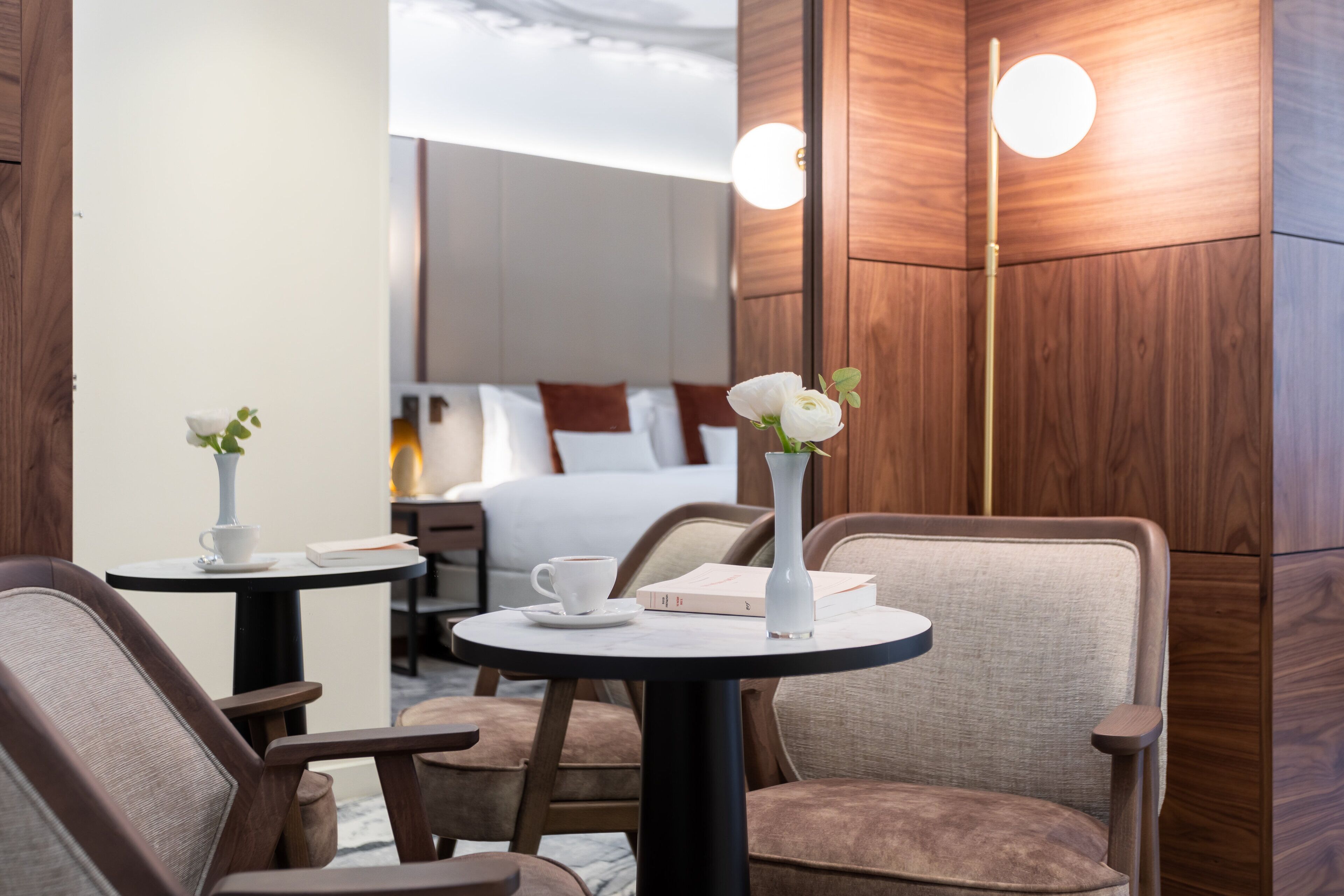 A hotel room with a bed, a small table with a vase and a cup, and two chairs.
