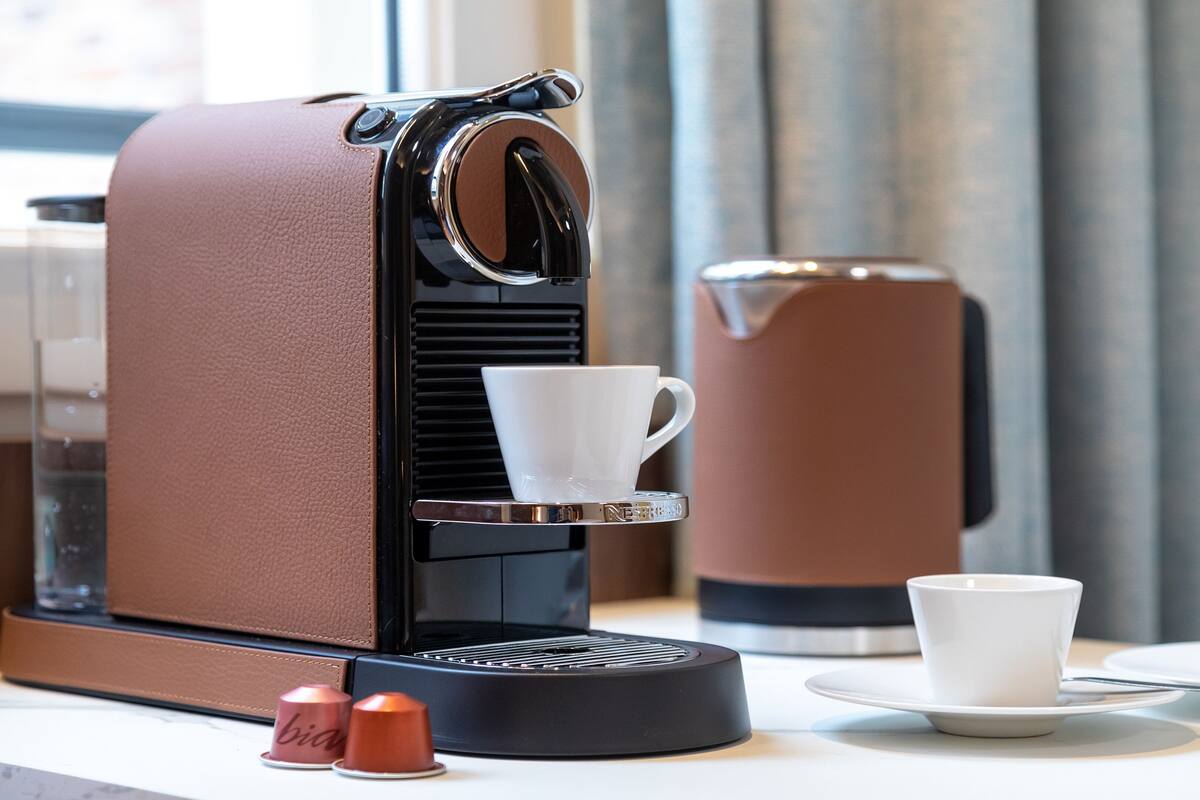 A coffee machine with a cup and saucer, a thermos, and a small container on a table.