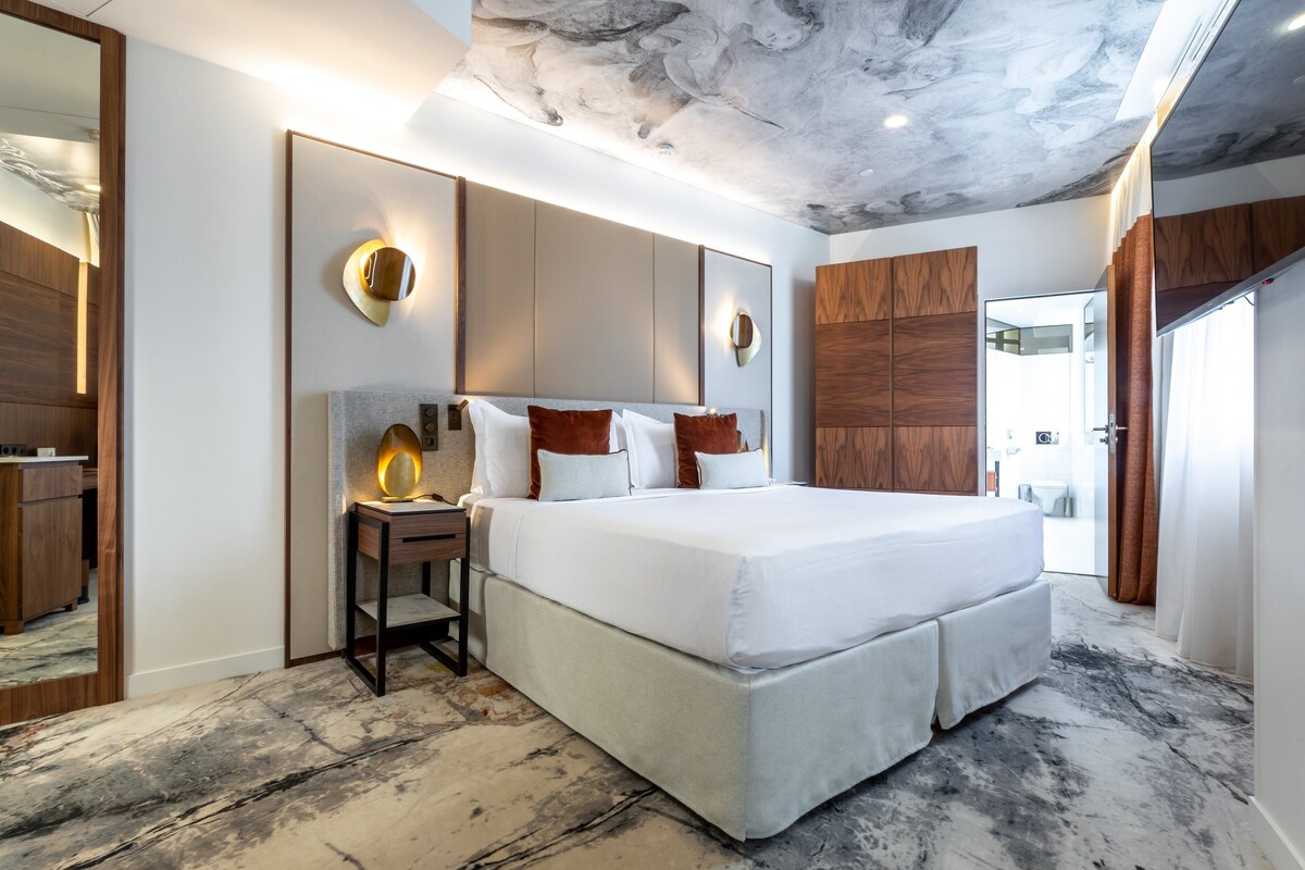 A modern hotel room with a large bed, a nightstand, a mirror, and a ceiling with a marble-like design.