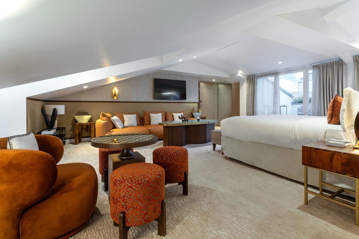 A hotel room with a large bed, a sofa, a desk, and a TV mounted on the wall.