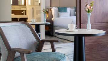 Una habitación de hotel moderna con una mesa redonda, un sillón cómodo, una cama con ropa de cama blanca y un jarrón con flores sobre la mesa.