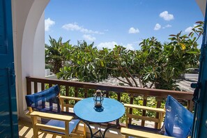 A balcony with a round table and two chairs, a lantern on the table, and a view of green foliage and a clear sky. - Petra Nera (Santorini)