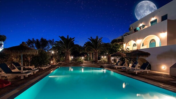 A nighttime pool area with lounge chairs and a large moon in the sky. - Petra Nera (Santorini)