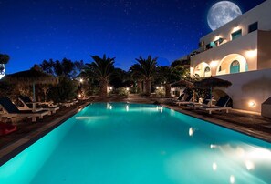 A nighttime pool area with lounge chairs and a large moon in the sky. - Petra Nera (Santorini)