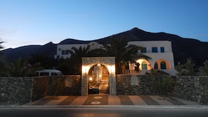 A building with a stone entrance, a mountain in the background, and palm trees. - Petra Nera (Santorini)