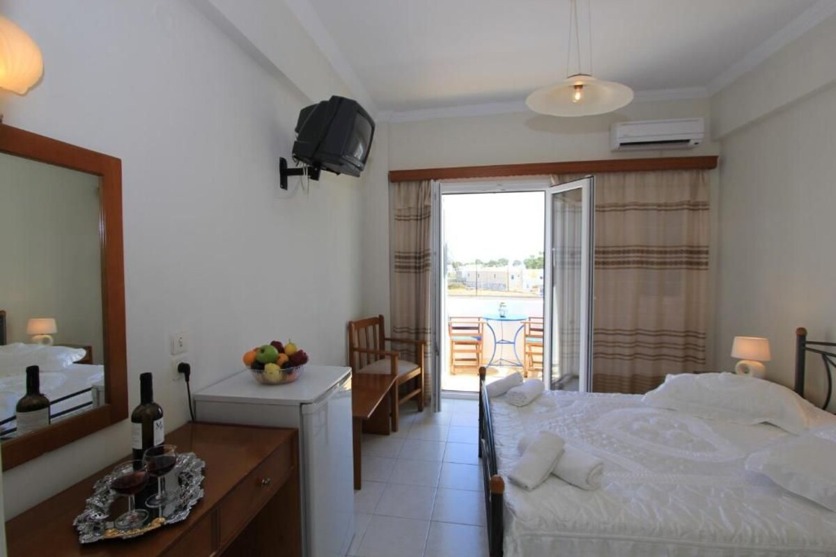 A hotel room with a bed, a desk with a fruit bowl, a TV, and a balcony with a table and chairs.