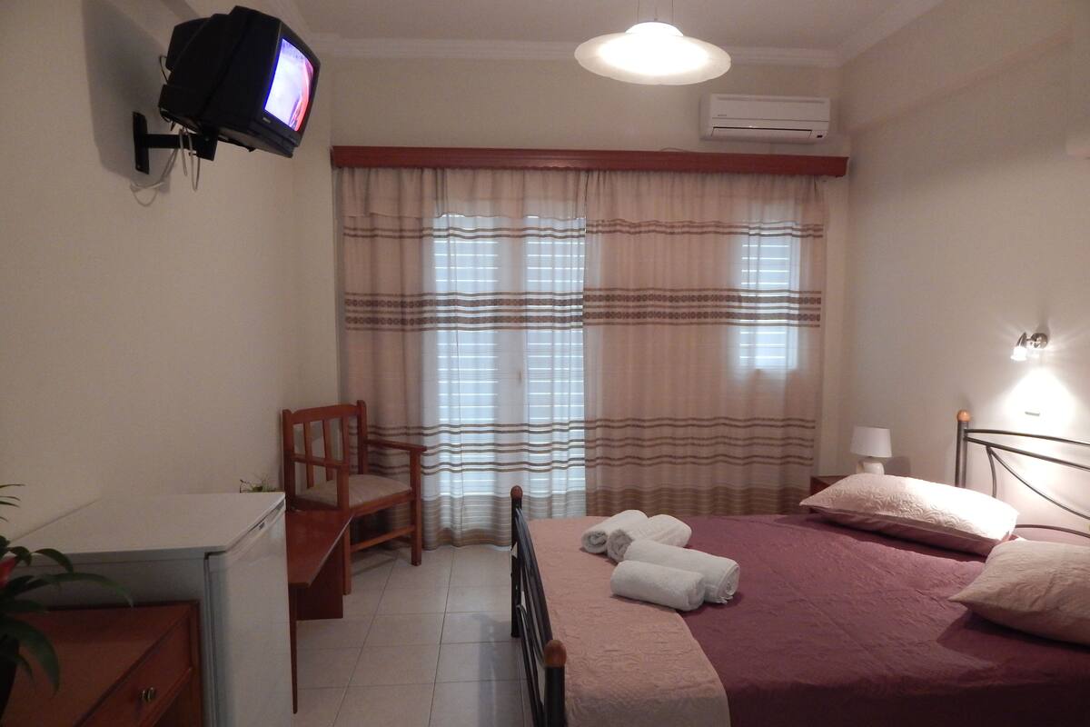 Habitació d'hotel amb llit, escriptori, cadira, televisió i finestra amb cortines.
