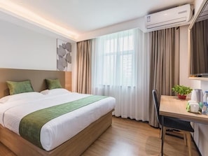 Habitación de hotel con cama, escritorio, silla, planta en maceta y aire acondicionado.
