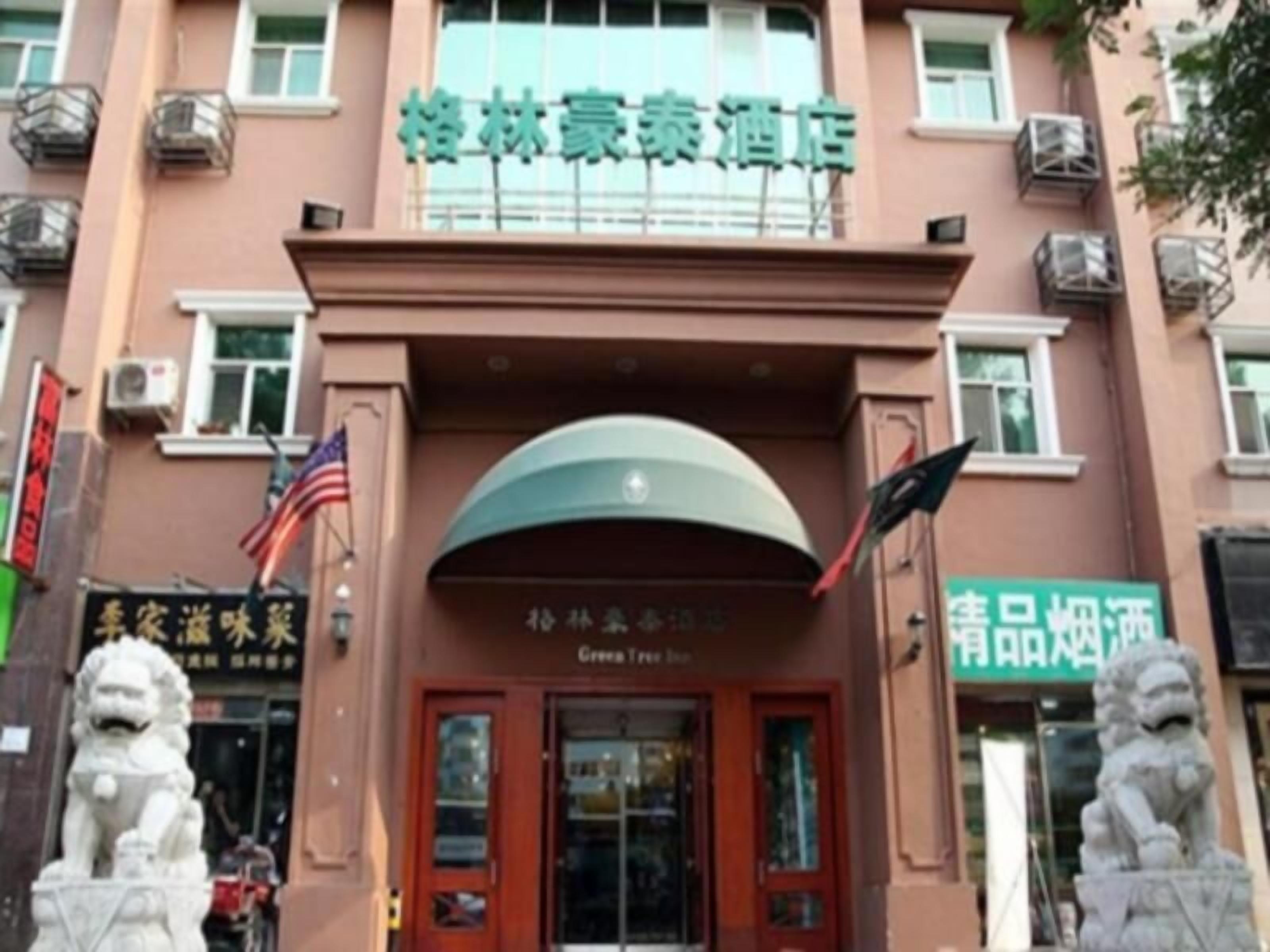 A hotel entrance with a green sign, two lion statues, and a red door.