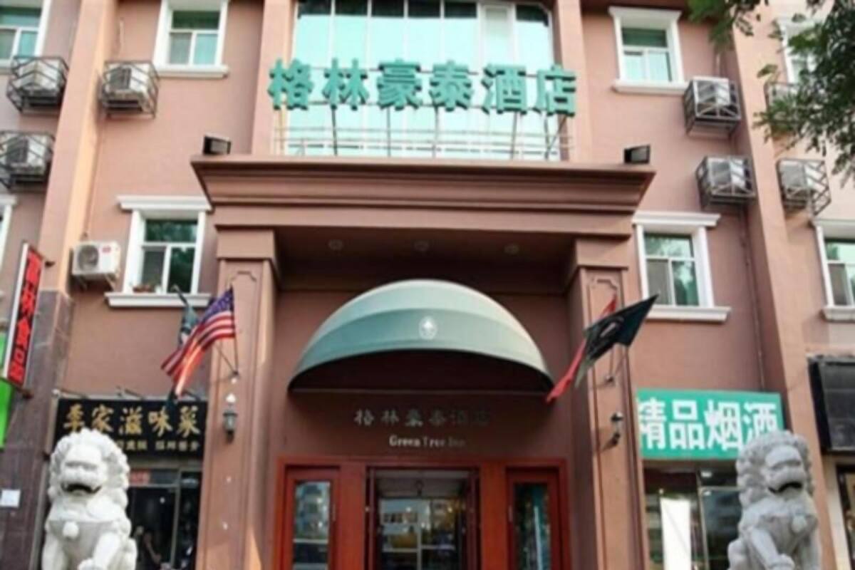 A hotel entrance with a green sign, two lion statues, and a red door.