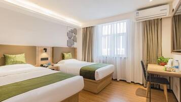 A hotel room with two beds, a desk, a chair, an air conditioning unit, and a window with curtains.