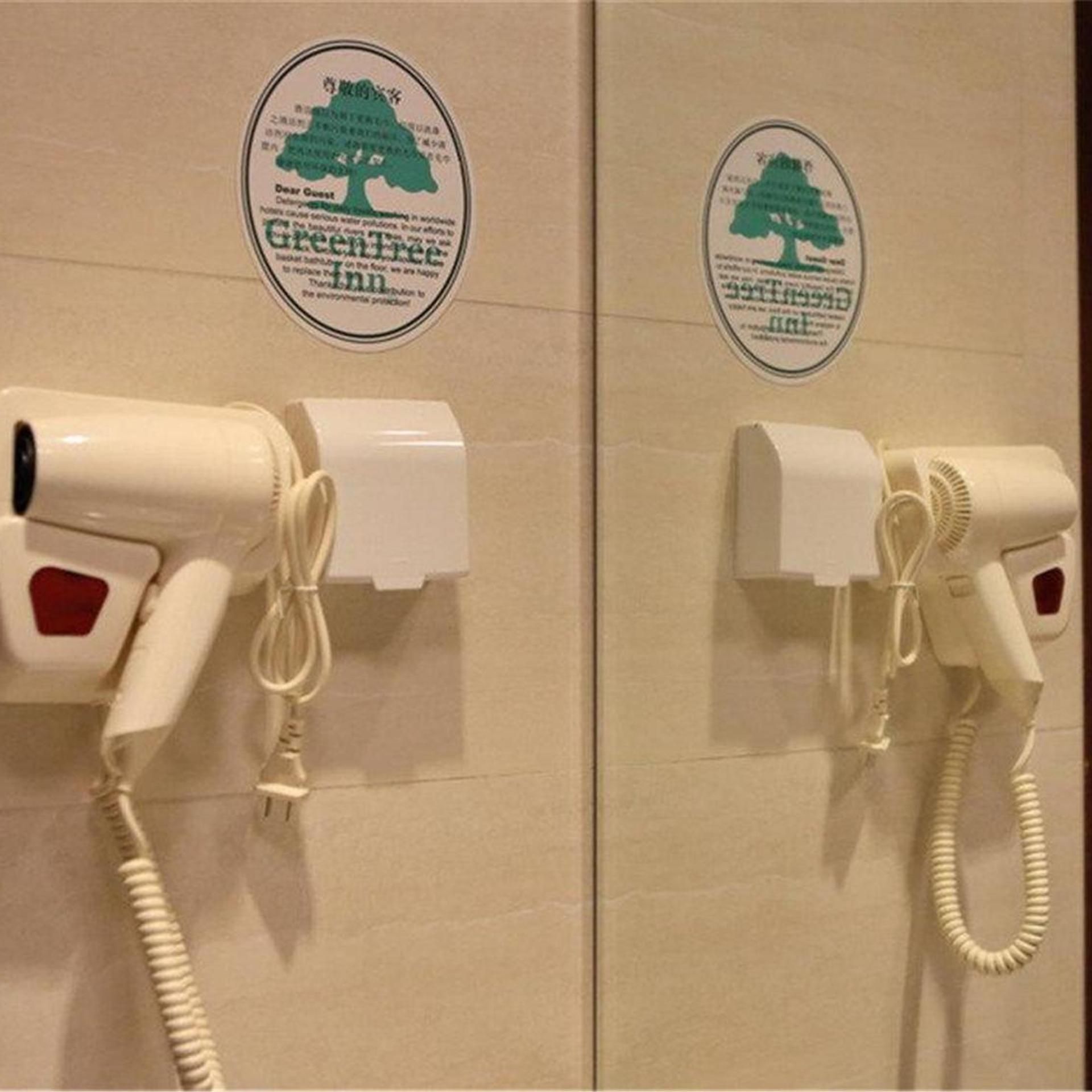 A restroom with two hair dryers mounted on the wall, each with a green tree logo sticker above them.