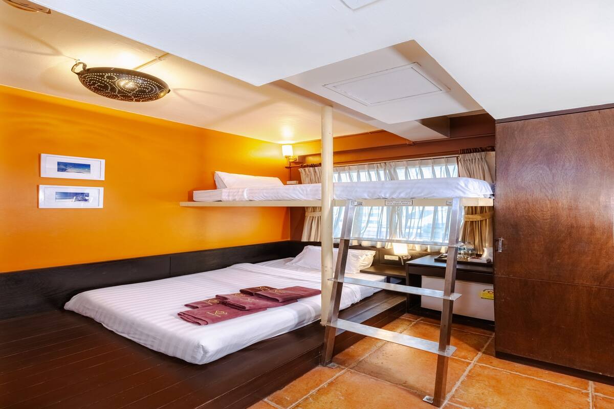 A hotel room with a bunk bed, a desk, a wardrobe, and a window with curtains.