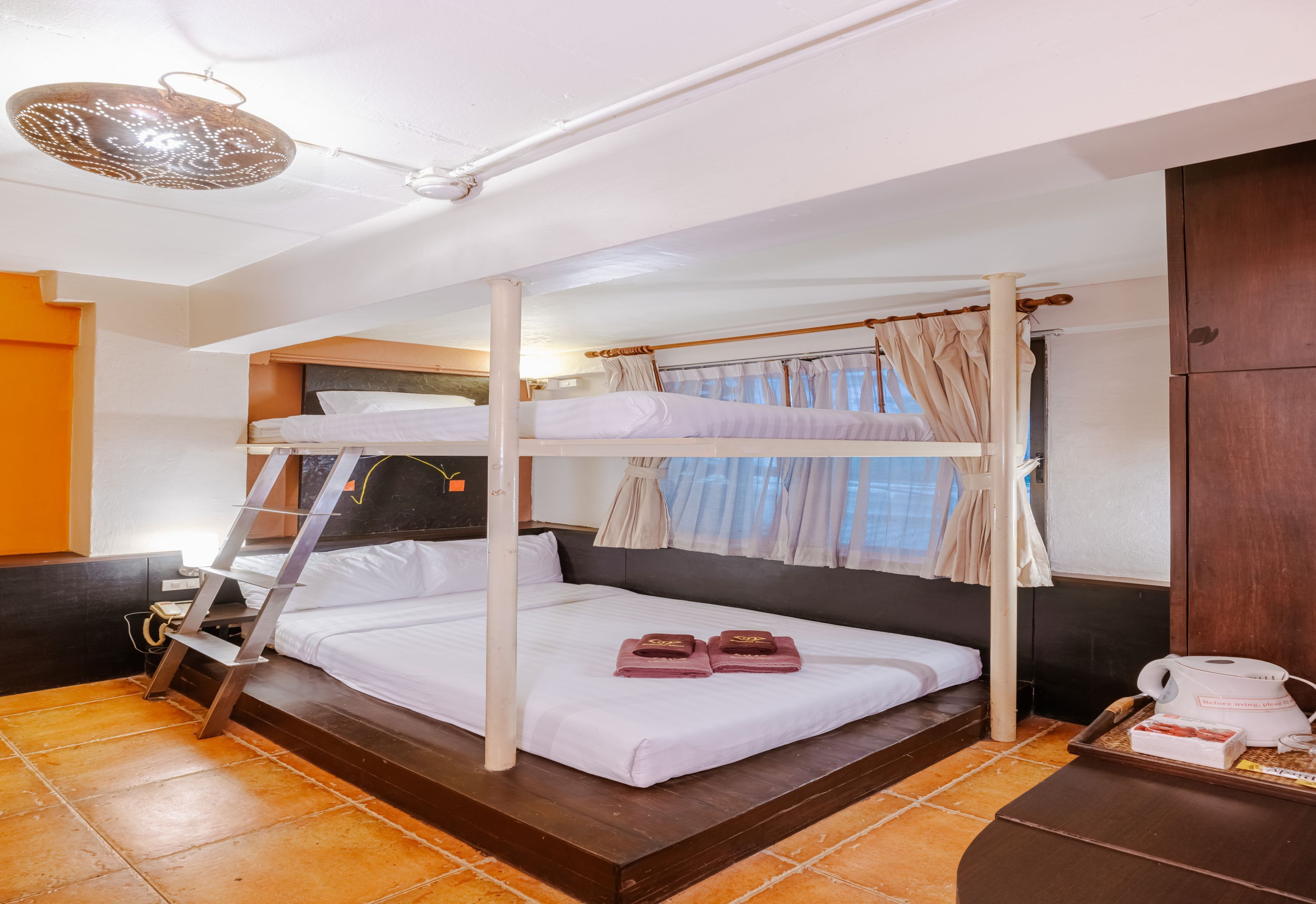 Habitación con literas, una escalera de madera, una mesita de noche con cafetera y una ventana con cortinas.