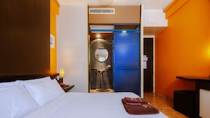 Une chambre d’hôtel avec un lit, une table de chevet, une salle de bain avec un miroir et un paravent bleu.