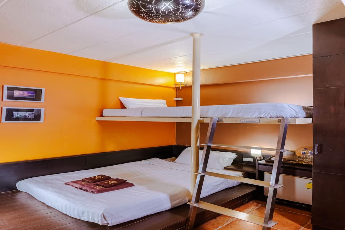 A bunk bed room with orange walls, a wooden floor, a ceiling light, and a small kitchenette.