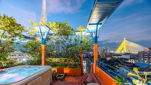Une terrasse sur le toit dotée d’un jacuzzi, de sièges en bois et offrant une vue sur le paysage urbain et un pont.