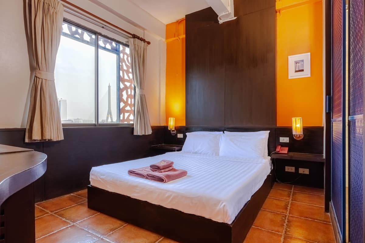 A hotel room with a bed, a desk, a window with curtains, and a wall-mounted light fixture.