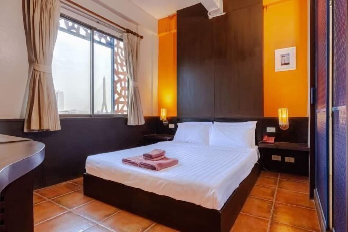 A hotel room with a bed, two bedside tables, a window with curtains, and a view of a cityscape.