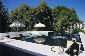 An infinity pool with lounge chairs and umbrellas, surrounded by trees and buildings. - M Glamour Hotel (Gabicce Mare)