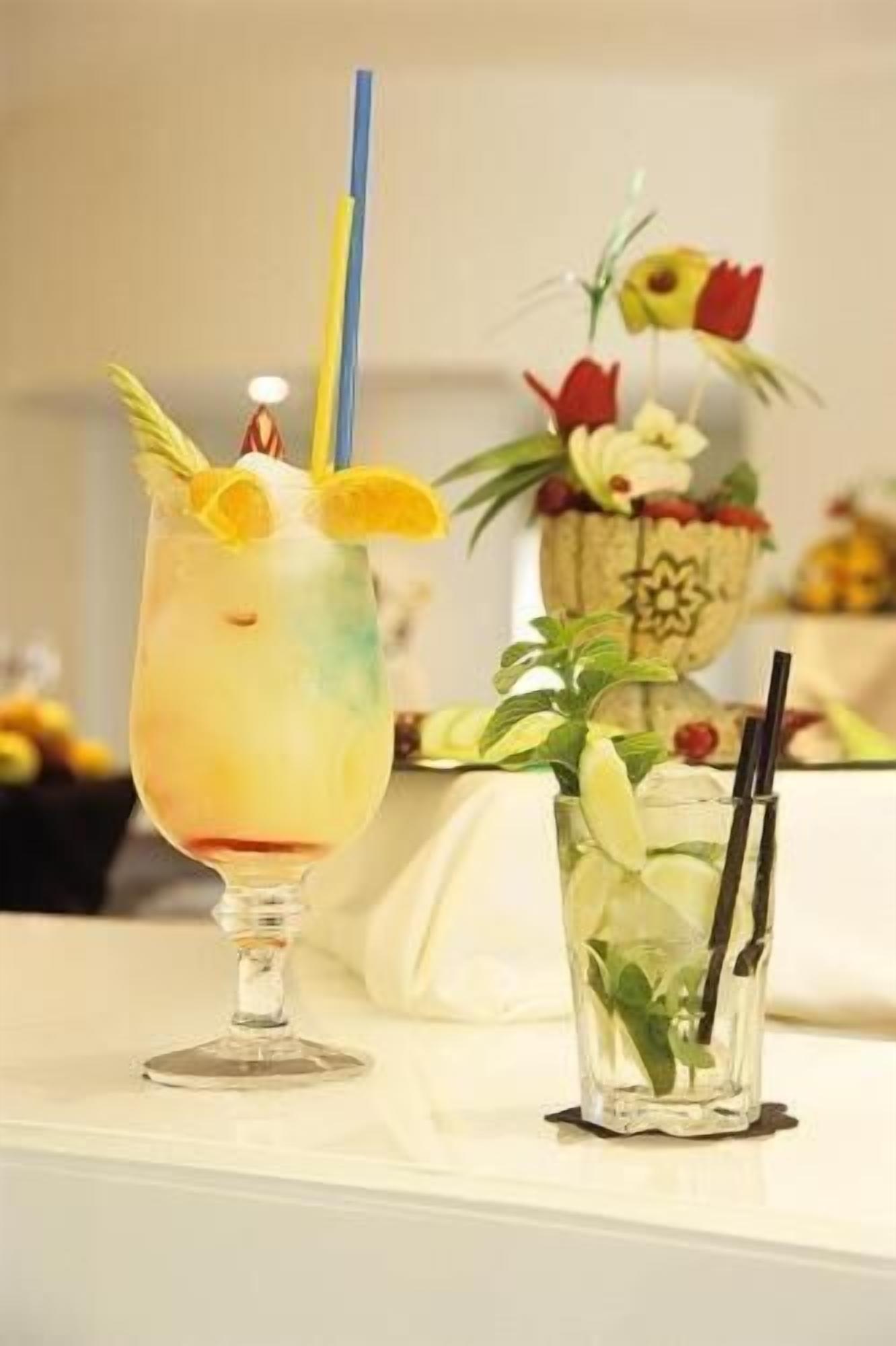 Dos bebidas sobre una mesa con un centro de mesa decorativo al fondo.
