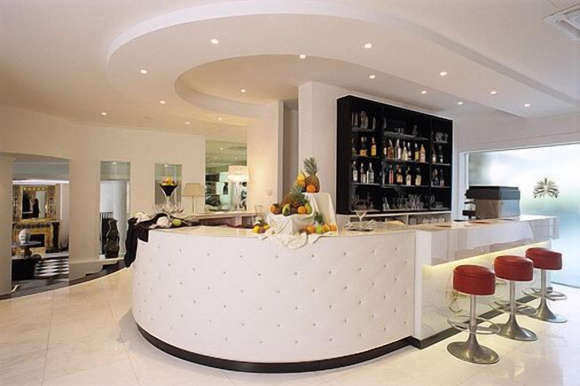 A modern hotel lobby with a curved reception desk, a bar area with stools, and a large bookshelf.