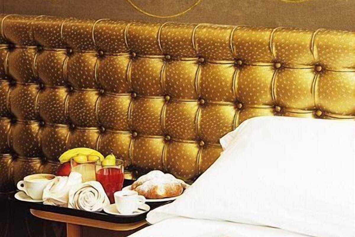 A luxurious hotel room with a tufted headboard, a tray with breakfast items, and a bed with a white comforter.