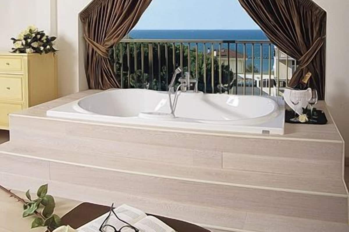 A modern bathroom with a large bathtub, a vanity, and a view of the sea.