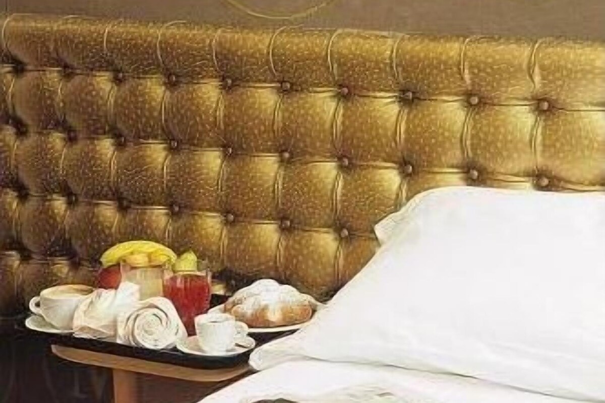 Una cama bien hecha con sábanas blancas y una bandeja de desayuno con pasteles y una taza.