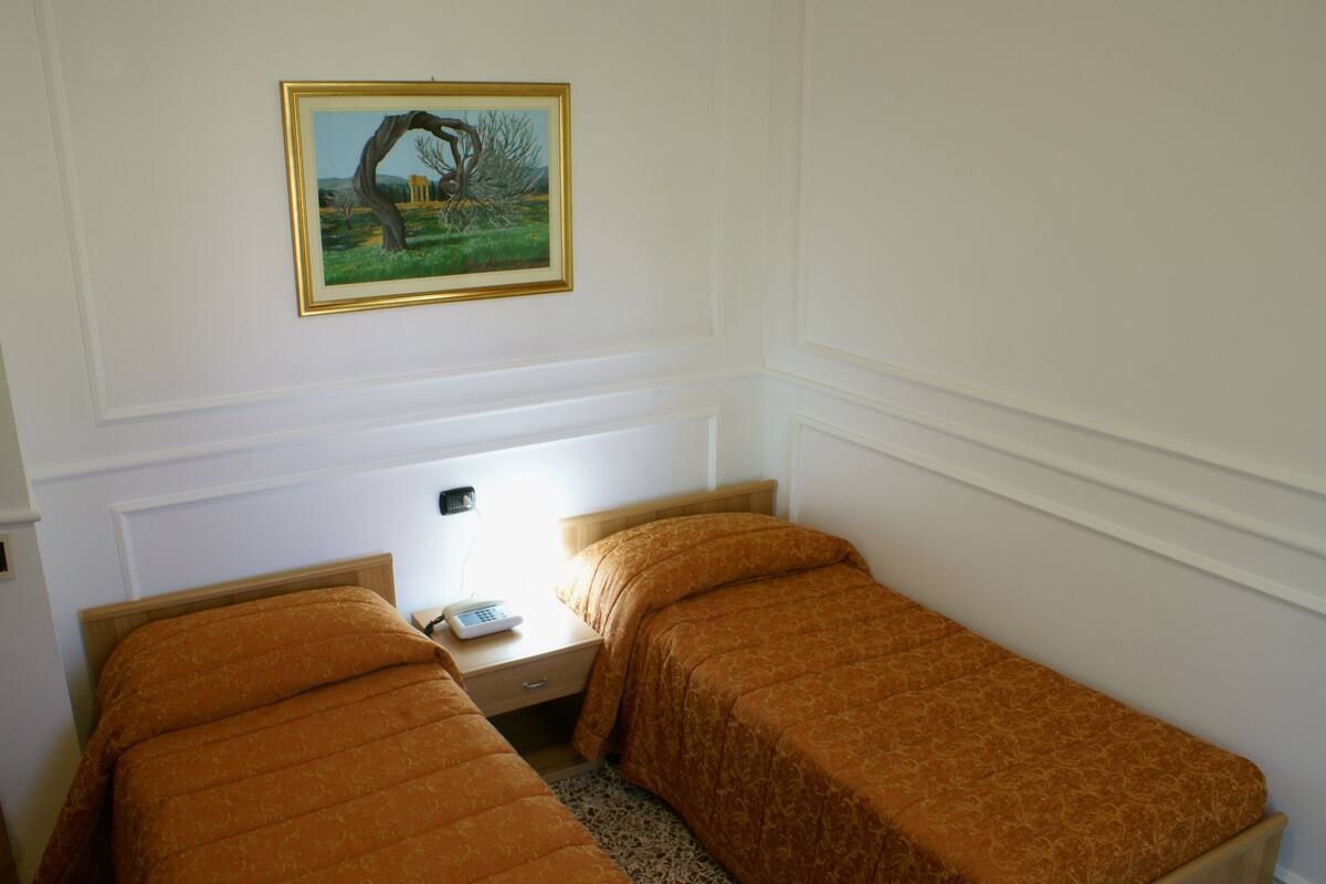 A twin room with two single beds, a bedside table with a lamp, and a framed picture on the wall.