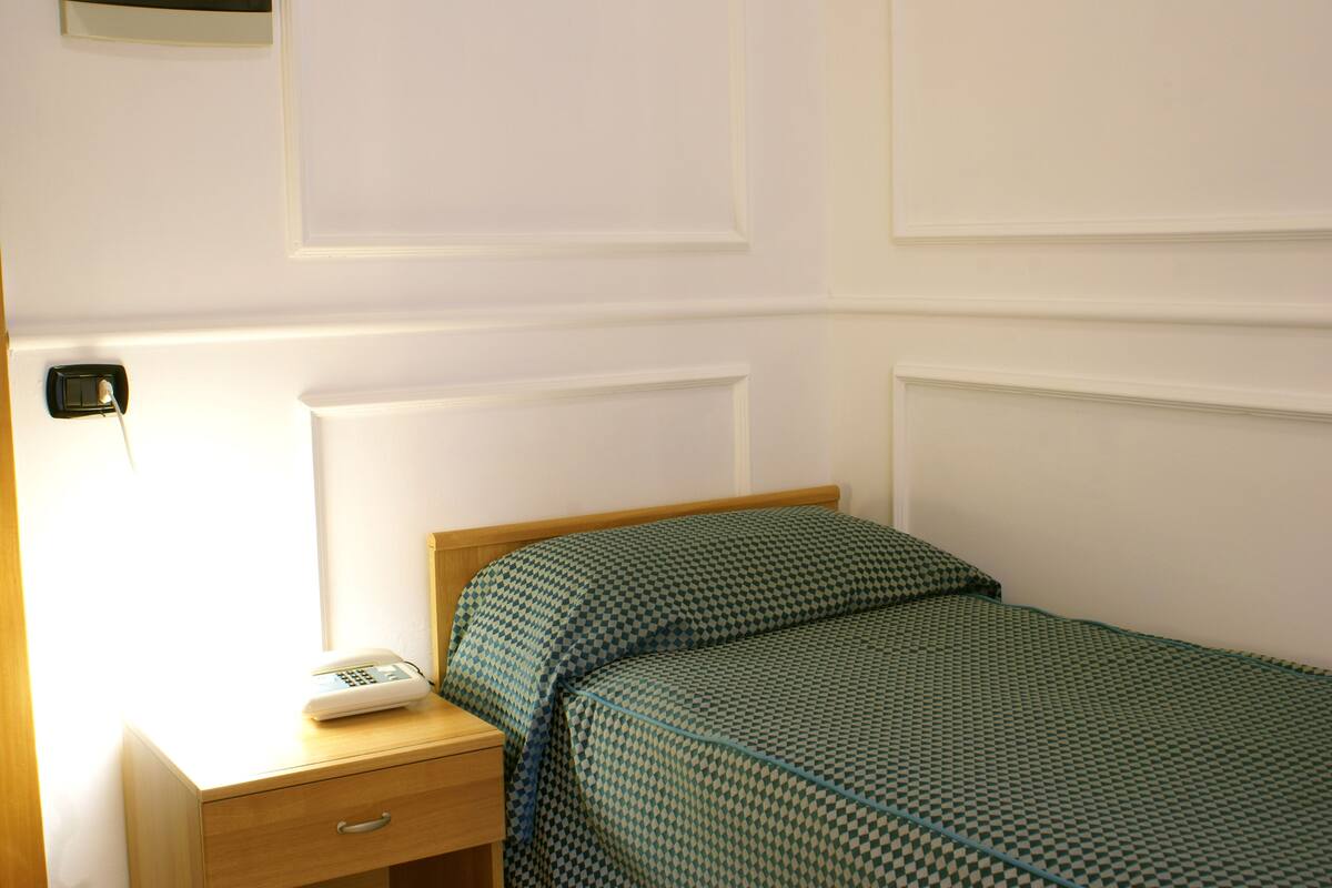 A neatly made bed with a checkered bedspread, a bedside table with a lamp, and a phone.