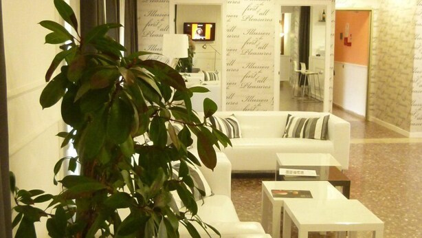 A modern lobby with a white sofa, a potted plant, and a patterned wall. - Hotel Amici (Agrigento)