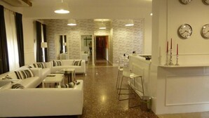 A modern living room with a sofa set, a coffee table, and a bar area with stools. - Hotel Amici (Agrigento)