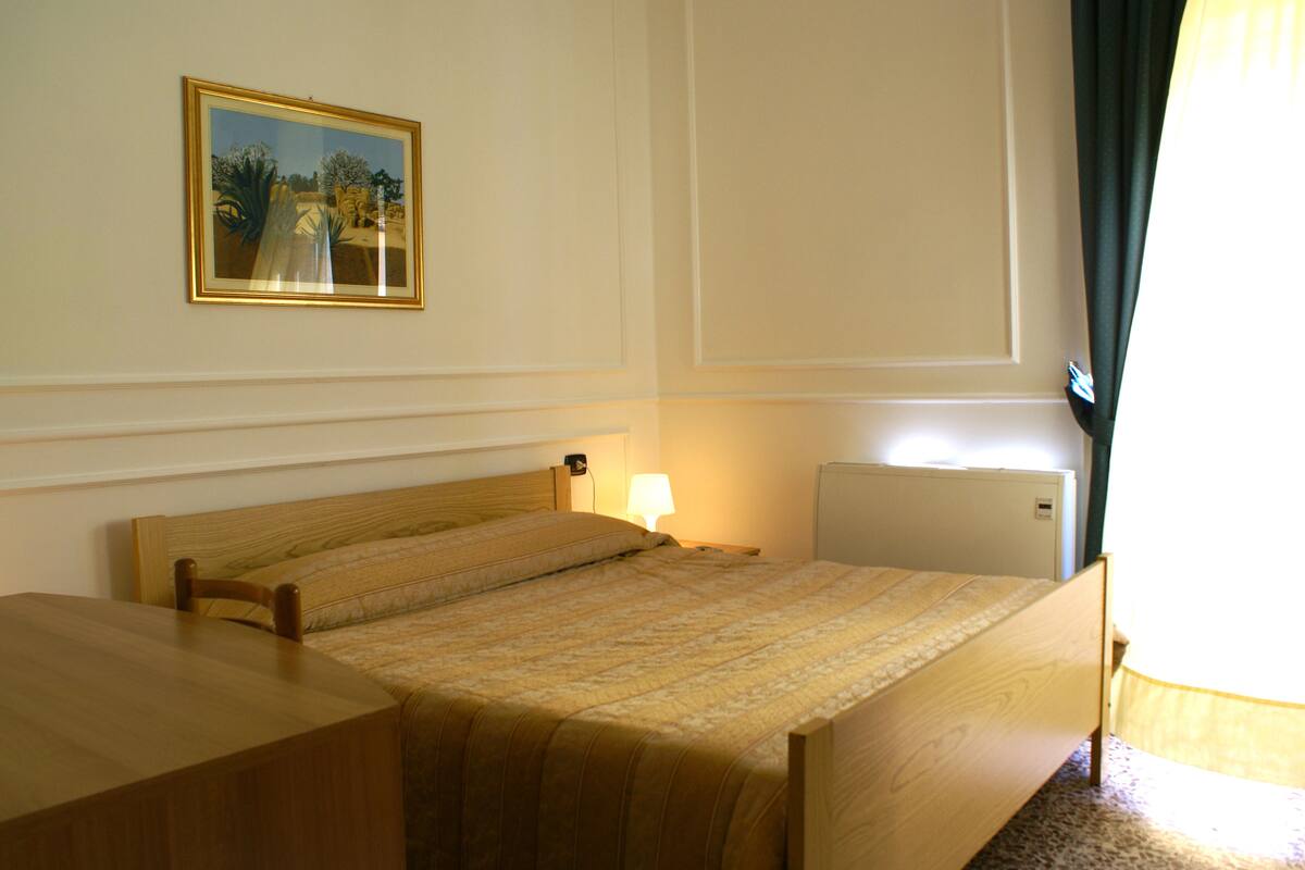 A hotel room with a single bed, a bedside table, a lamp, and a radiator.