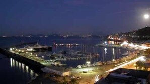 A marina at night with boats docked, a pier with lights, and a building with illuminated windows. - Hotel Il Nespolo (Casamicciola Terme)