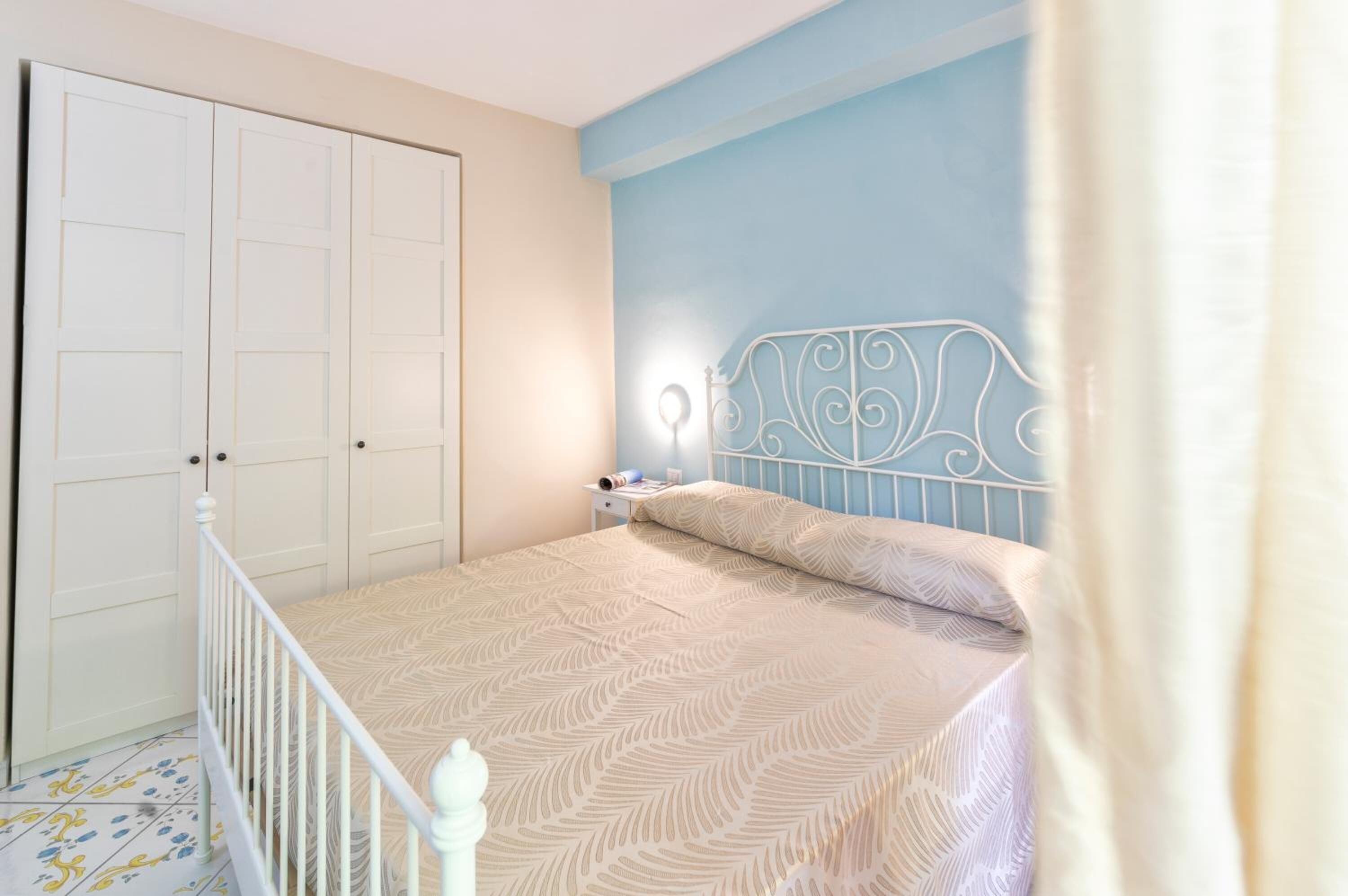 Un dormitorio con cama, mesita de noche, armario y cortina.