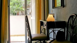 A room with a chair, a table with a lamp, a mirror, and a door leading to an outdoor area with curtains. - Hotel Il Nespolo (Casamicciola Terme)