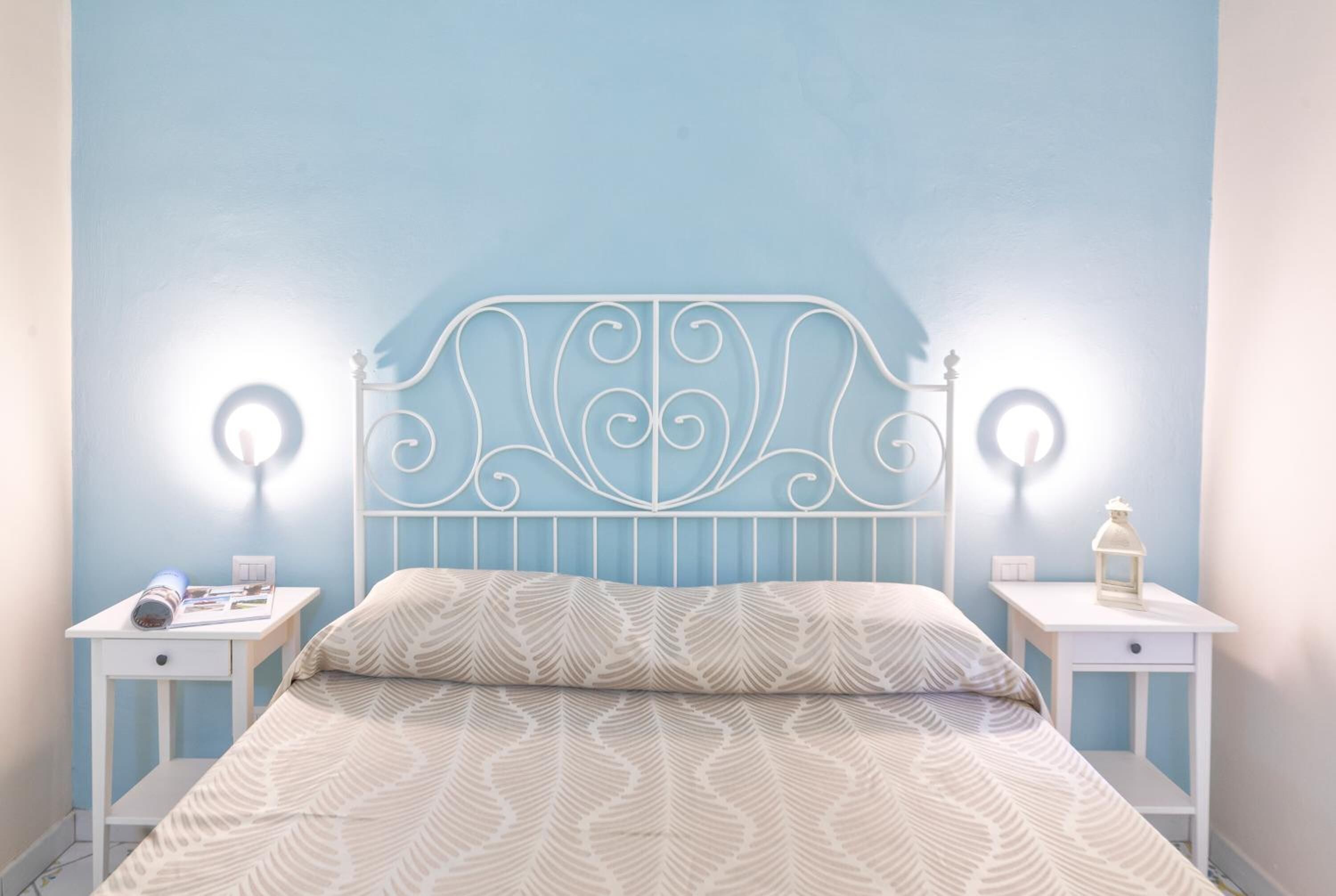A bedroom with a bed, two bedside tables, and wall-mounted lights.