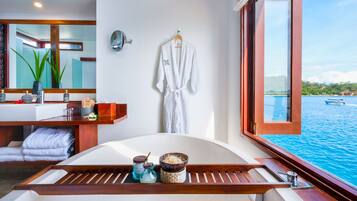Une salle de bain moderne avec une baignoire, un porte-serviettes et une grande fenêtre donnant sur un plan d’eau.