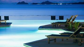 Zona de piscina con sillones de descanso y vista al océano al atardecer.