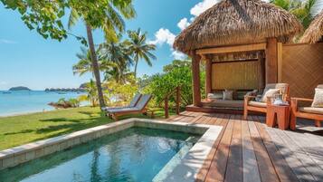 A poolside area with a thatched-roof structure, lounge chairs, and a view of the ocean.