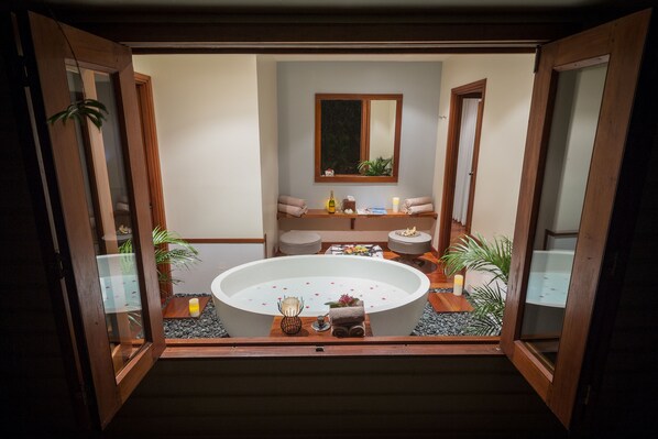 A spa room with a large bathtub, wooden furniture, and potted plants.