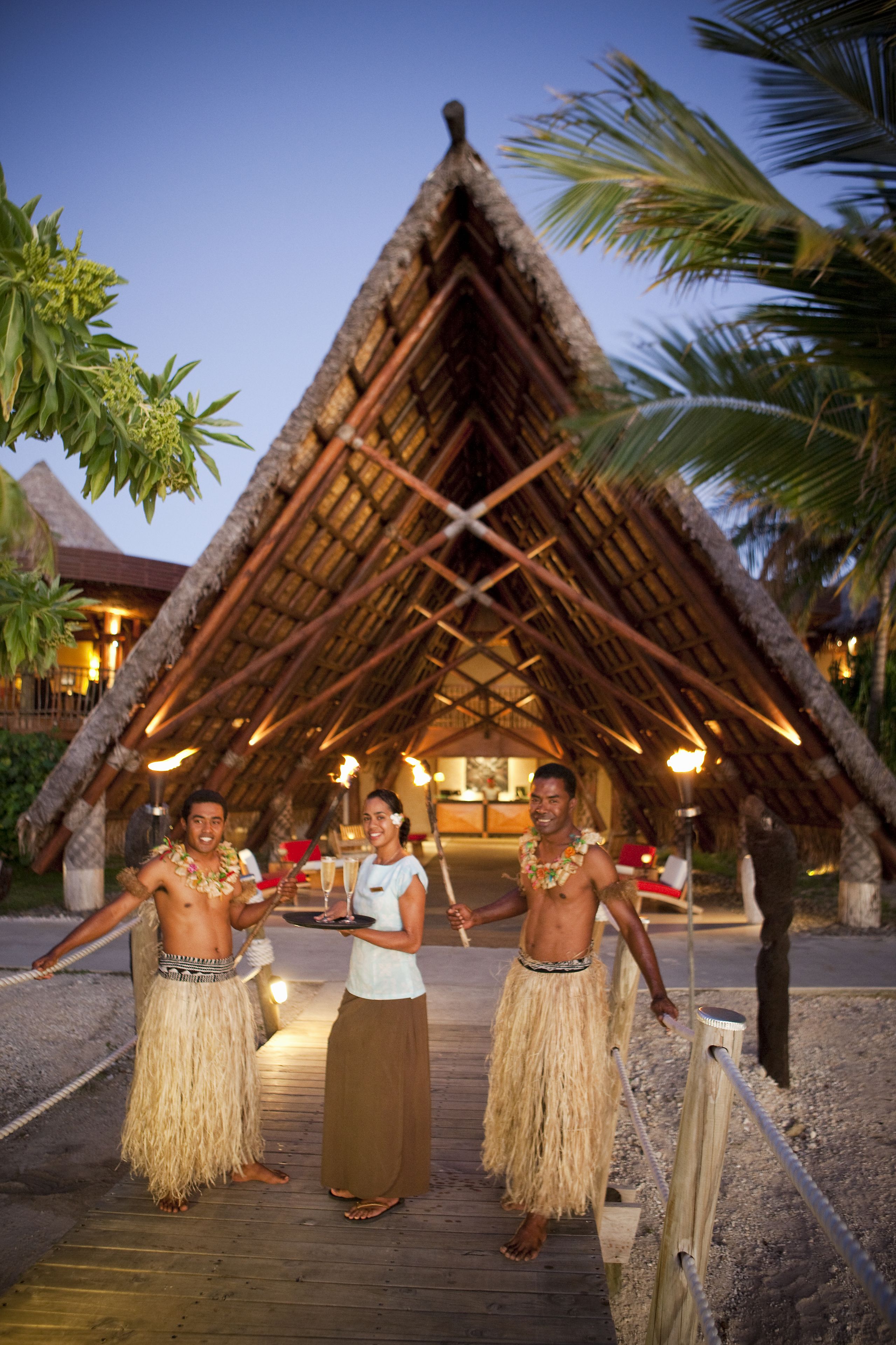A thatched-roof structure with a wooden deck in front, surrounded by palm trees.