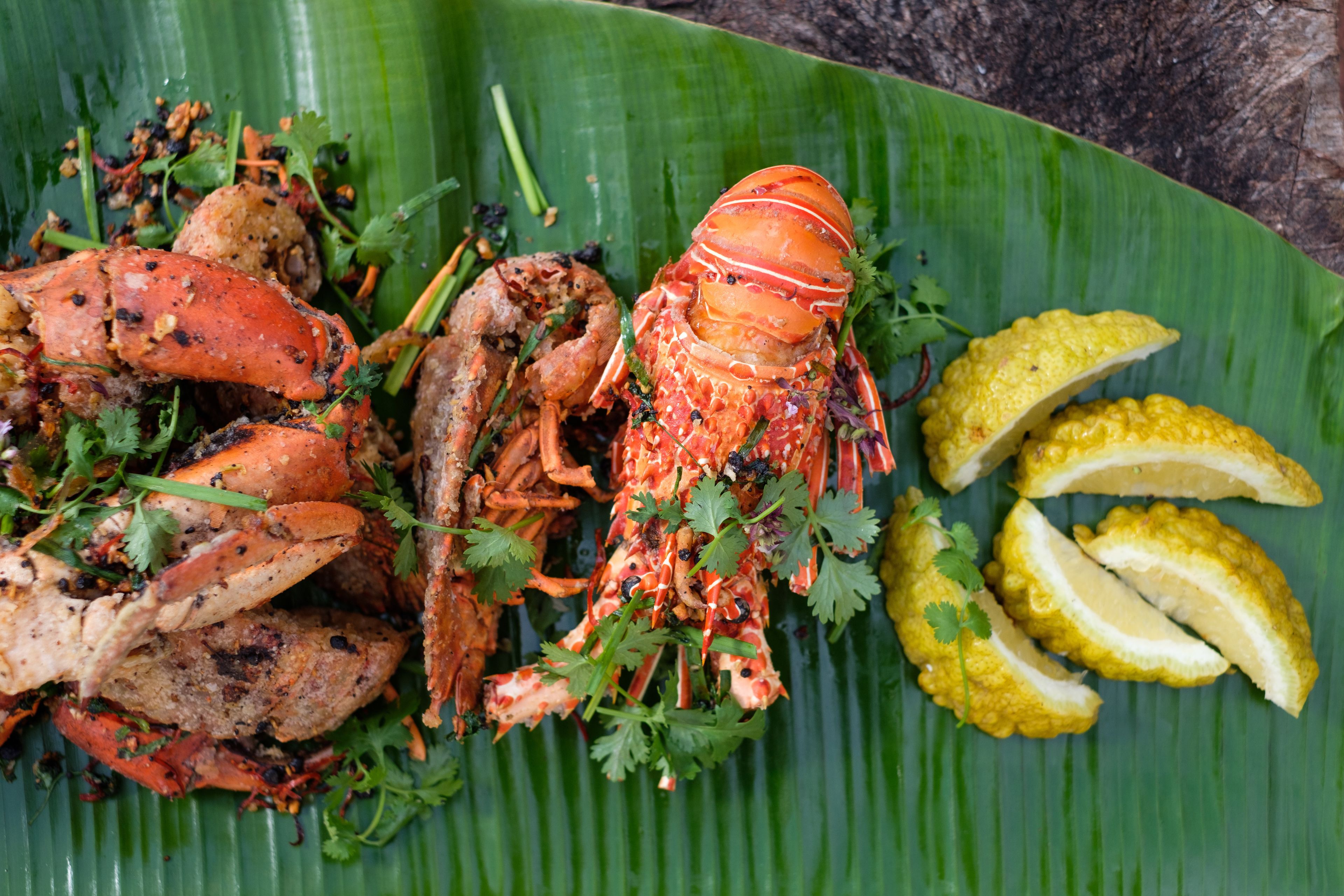 A plate of grilled seafood, including lobster and shrimp, garnished with herbs, served on a banana leaf.