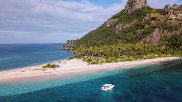 Une plage aux eaux turquoise et limpides, un bateau et un paysage montagneux à la végétation luxuriante.